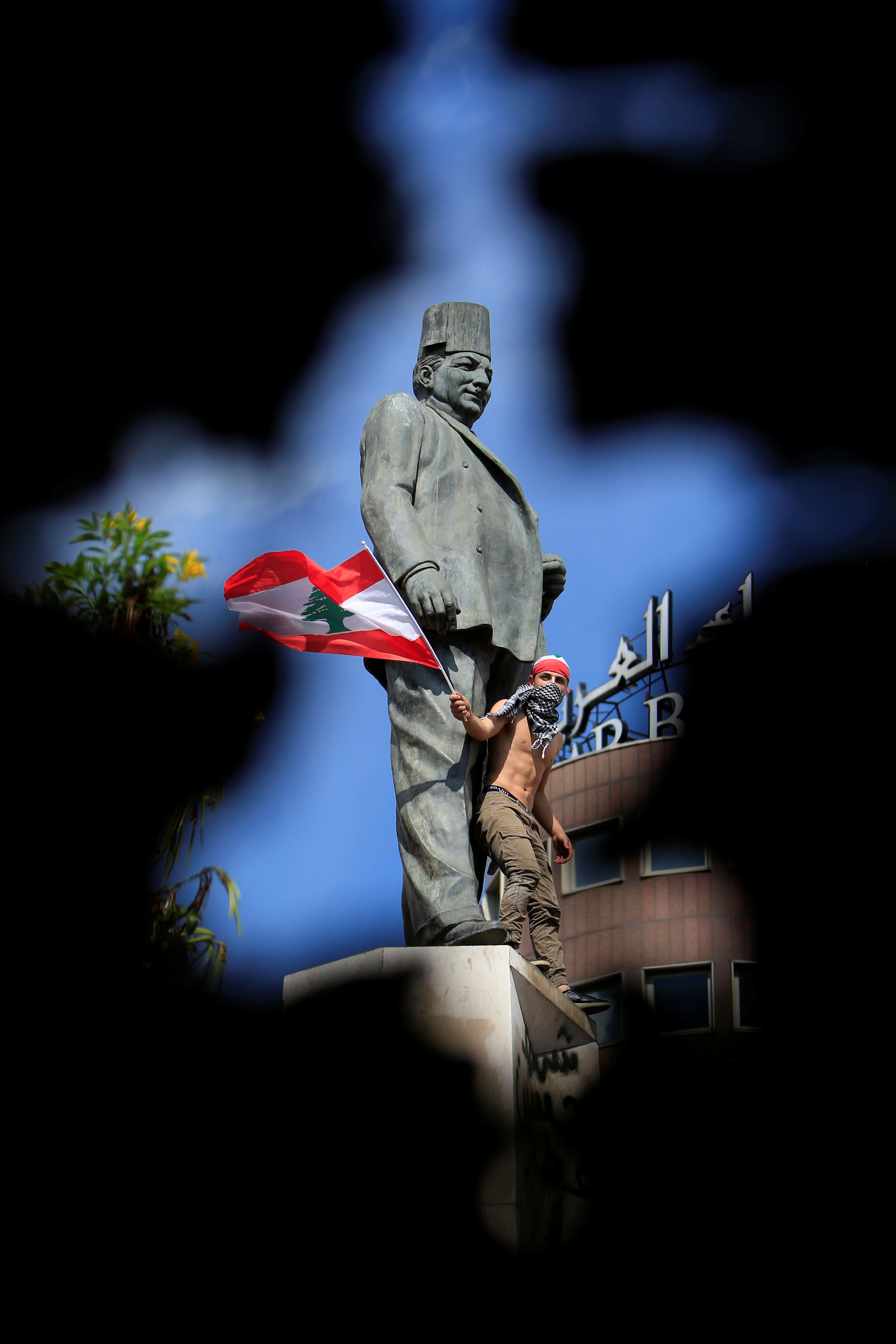 متظاهر يلوح بعلم وطني وهو يقف في تمثال رياض الصلح