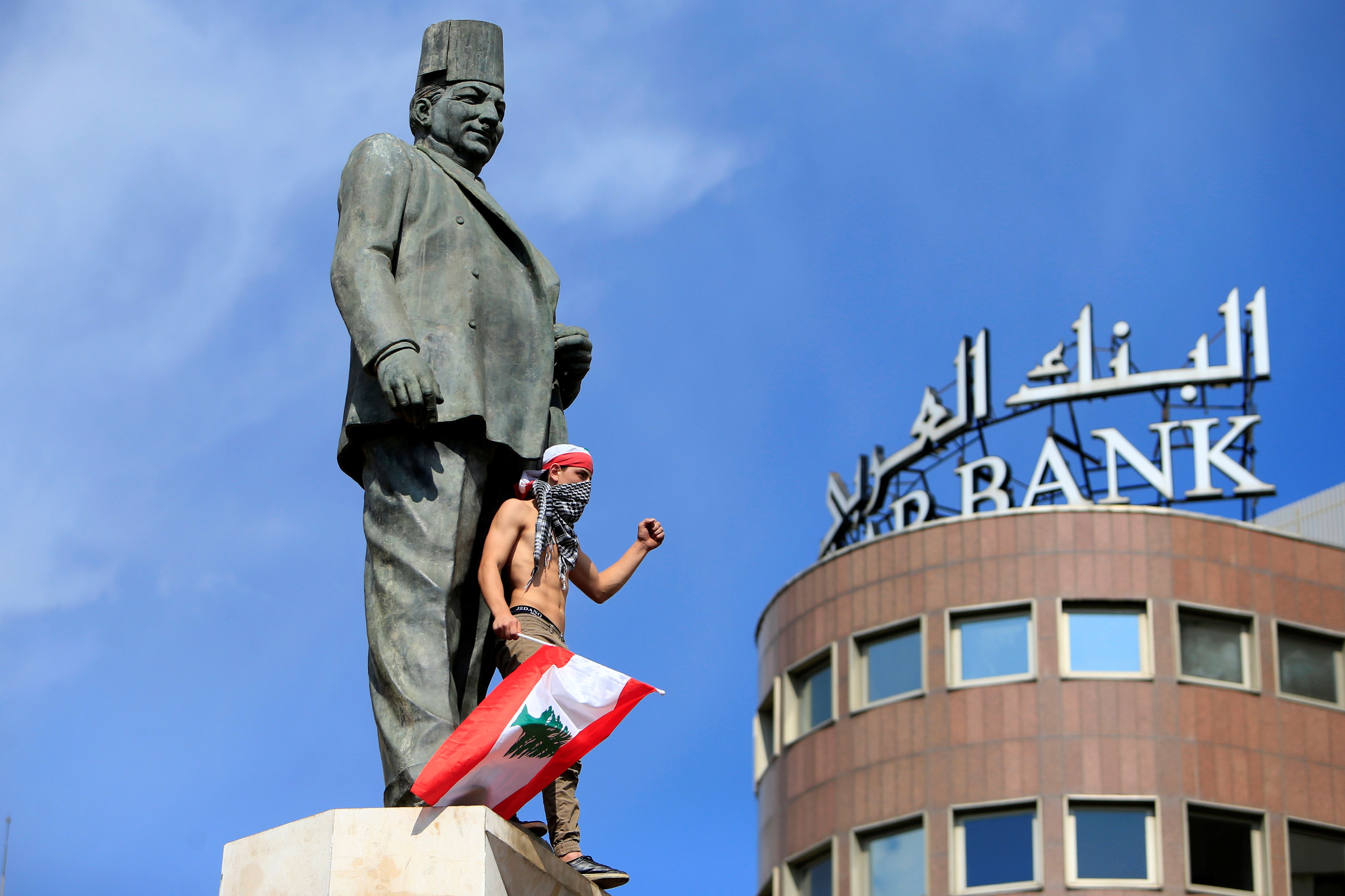 أحد المتظاهرين يلوح أثناء وقوفه في تمثال رياض الصلح بوسط بيروت
