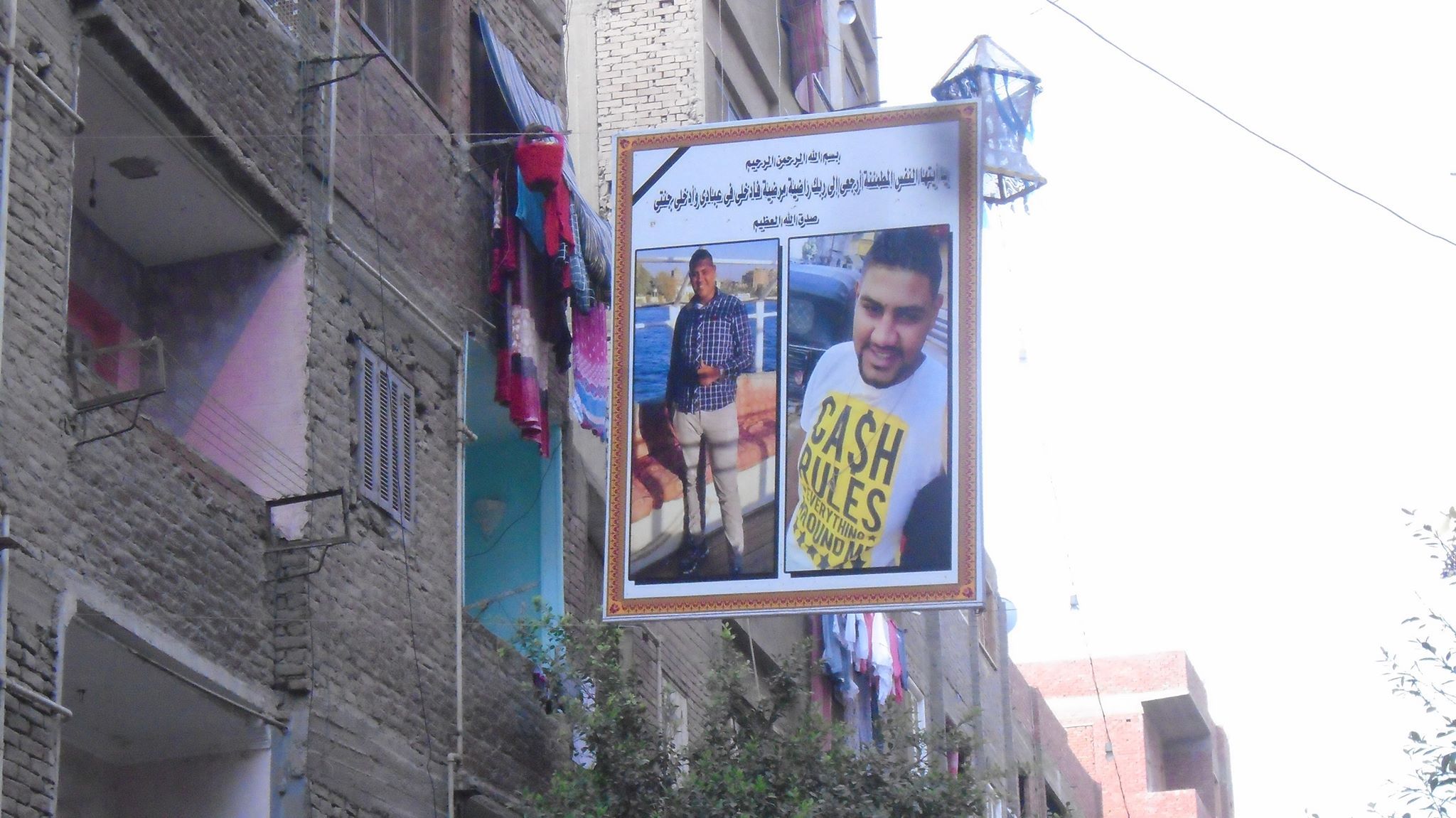 جيران الضحية واصدقائه يعلقون لافتة بالشارع تحمل صورة الضحية