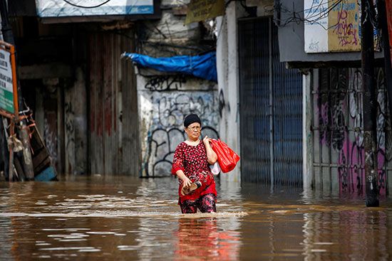 63969-امرأة-تحمل-متعلقاتها-تسير-عبر-مياه-الفيضان