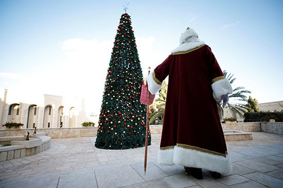 رجل يرتدى زى سانتا كلوز يسير بجوار شجرة عيد الميلاد
