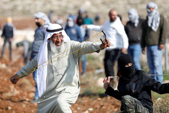 رجل فلسطيني يلقى الحجارة على جنود الاحتلال