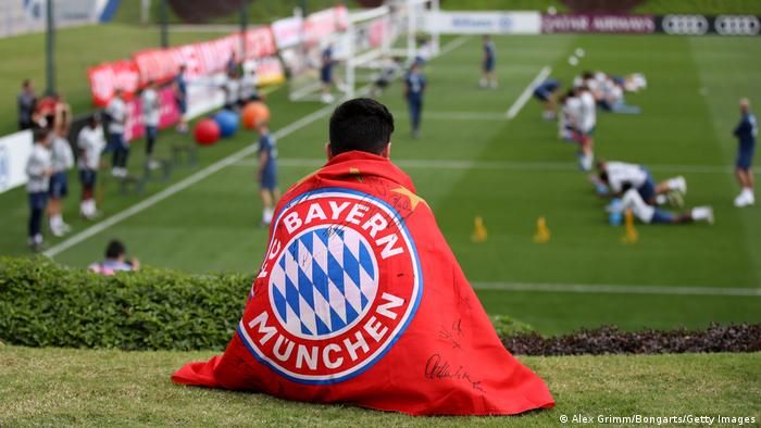 A Bayern Munich fan watches training in Qatar with a Bayern flag wrapped around him.