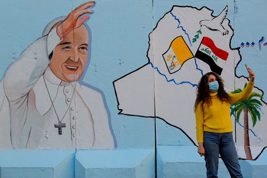فتاة تلتقط صور سيلفي مع جدارية للبابا فرنسيس على جدار إحدى الكنائس في بغداد